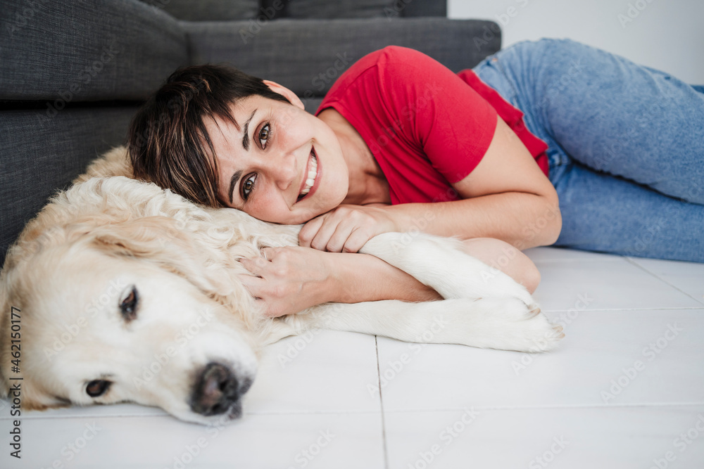 Smiling mid adult woman lying with dog on floor at home Smiling mid adult woman lying with dog on floor at home