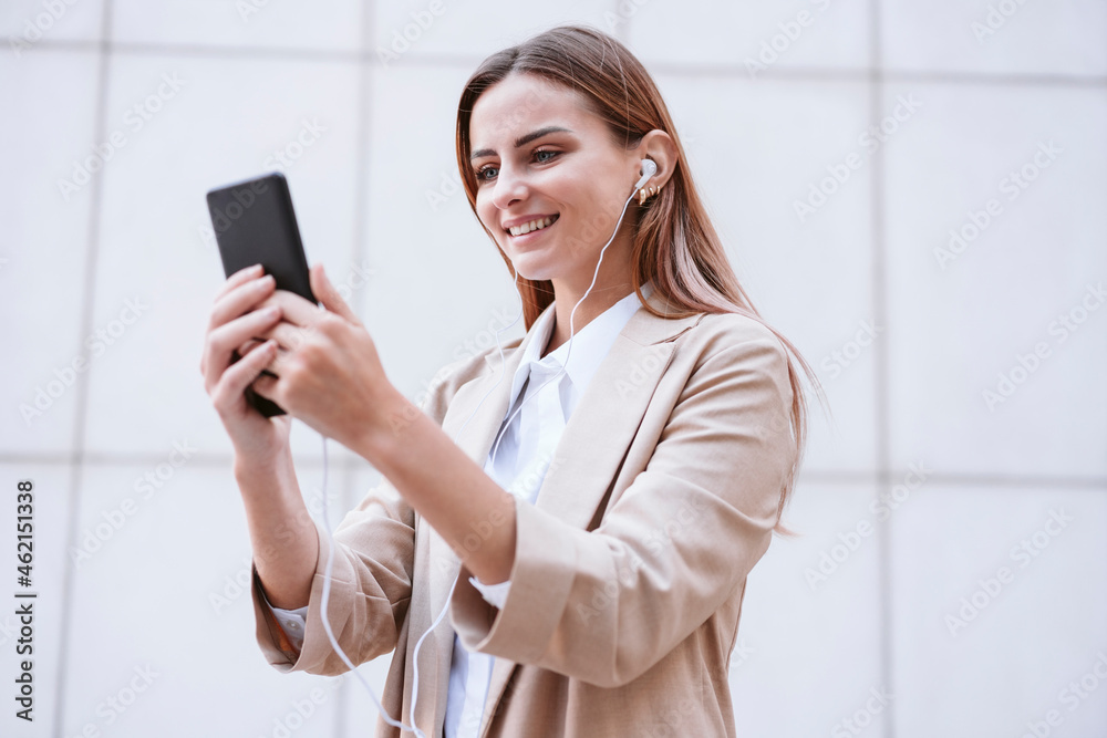 Businesswoman smiling while doing video call through smart phone in front of wall Businesswoman smiling while doing video call through smart phone in front of wall