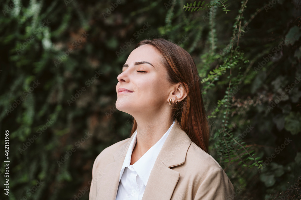 Businesswoman with eyes closed at green plant wall Businesswoman with eyes closed at green plant wall