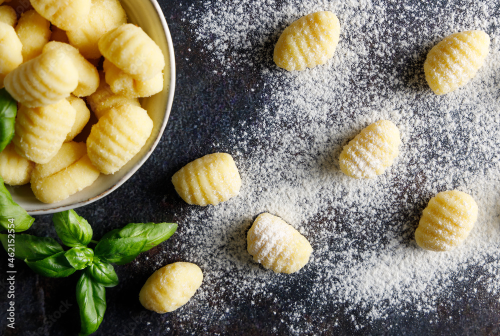 Homemade italian gnocchi. Fresh homemade uncooked gnocchi Italian dumplings on a floured wooden board in a kitchen with fresh basil,potatoes and wheat flour behind .