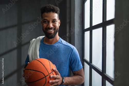 Happy young African American basketball player standing indoors at gym, looking at camera.