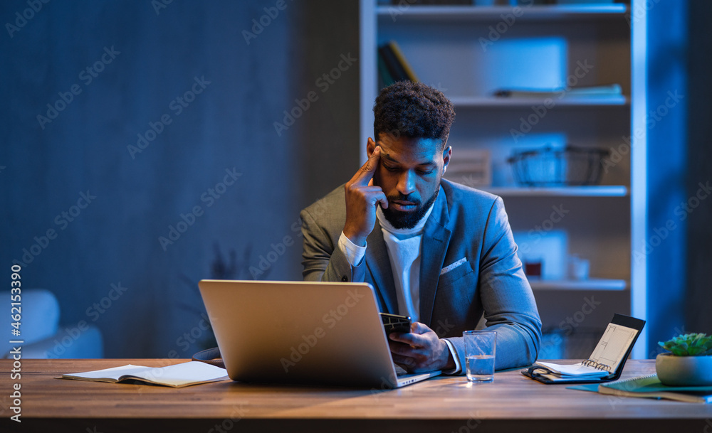 Young african american businessman working indoors in office at night. Young african american businessman working indoors in office at night.