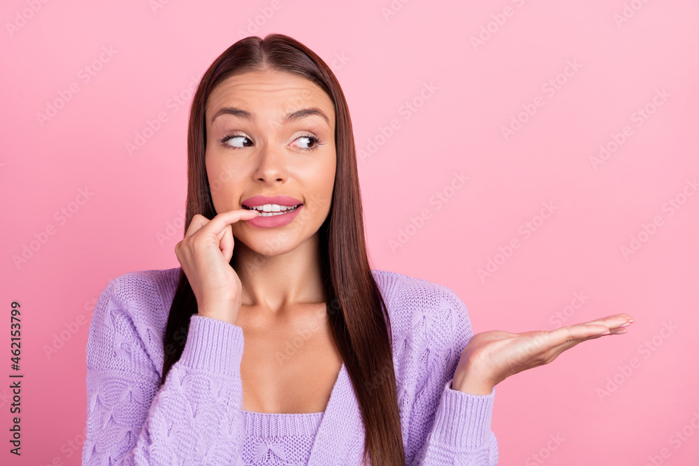Photo of young doubtful curious woman hold hands empty space bite finger nail isolated on pink color background Photo of young doubtful curious woman hold hands empty space bite finger nail isolated on pink color background