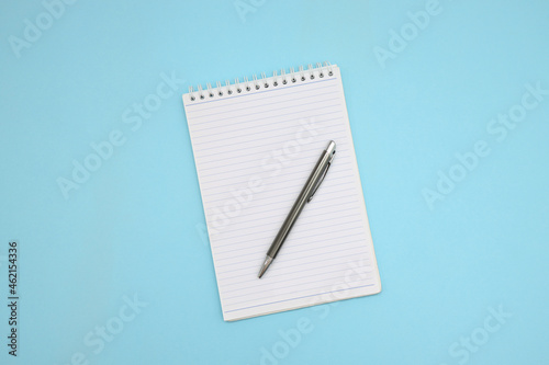 Top view of spiral blank note with silver pen on top against blue background