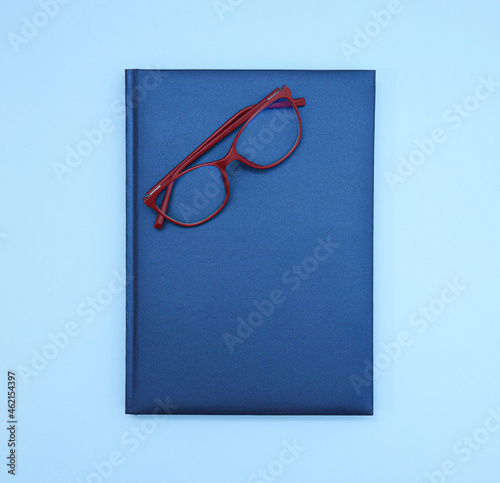 Close up view of isolated blue hard cover notebook with red glasses on top. Copy space 