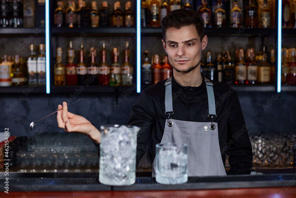 Barman stirring ice cubes in cocktail glass with spoon