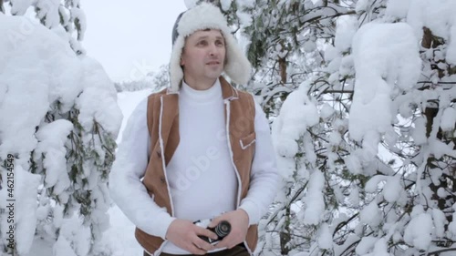 Traveling man with retro photo camera and in warm clothes walking in winter forest among trees covered with snow 