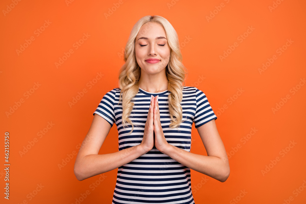 Portrait of attractive cheerful grateful hopeful wavy-haired girl praying sincerely isolated over bright orange color background Portrait of attractive cheerful grateful hopeful wavy-haired girl praying sincerely isolated over bright orange color background