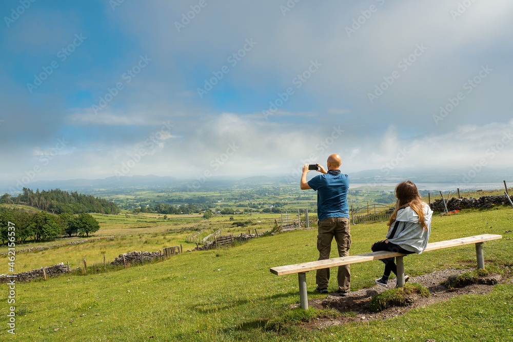 Father and daughter spend time together on a bench in a park with great scenery view Bald father and teenager girl outdoors. One parent or divorced family concept. Warm sunny day, cloudy sky.