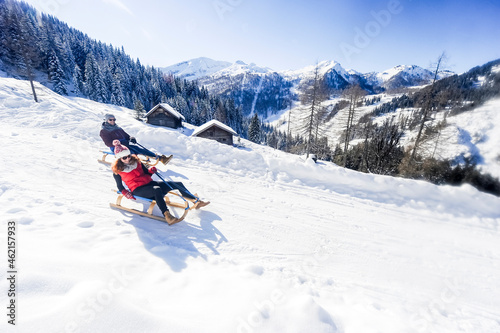 Playful couple sledding on snow during winter photo