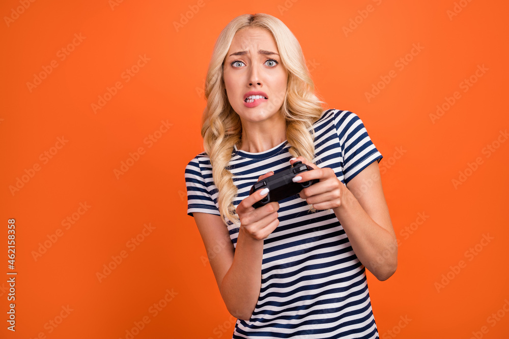 Portrait of attractive addicted worried girl playing game worrying biting lip weekend isolated over bright orange color background Portrait of attractive addicted worried girl playing game worrying biting lip weekend isolated over bright orange color background