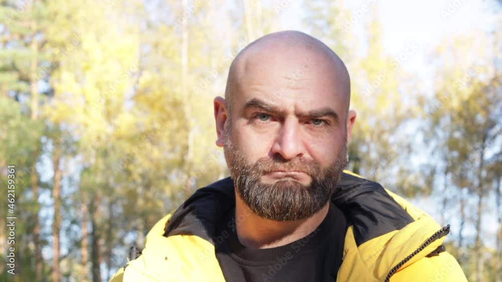 Bearded man in yellow jacket looking frowning outside in the autumn park on the background Bearded man in yellow jacket looking frowning outside in the autumn park on the background