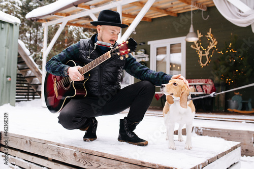 Seasoned musician in a hat and leather jacket patting a dog on the head