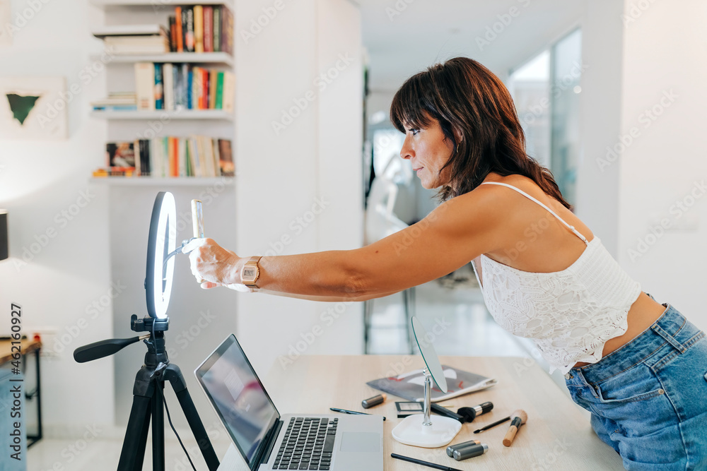 Female vlogger adjusting smart phone on ring light while standing at home Female vlogger adjusting smart phone on ring light while standing at home