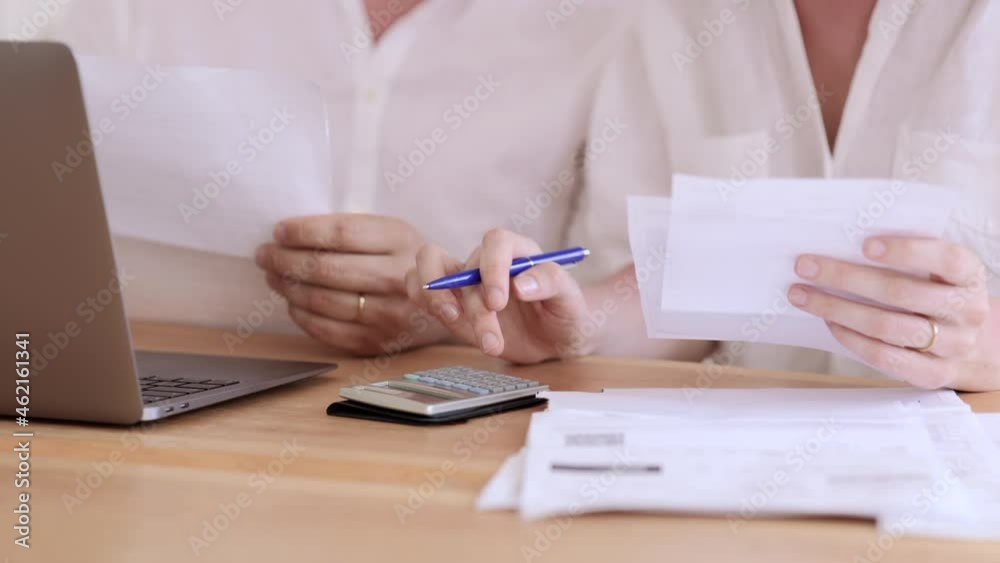 Woman counting on calculator and man working with laptop while sitting at table in home room spbi. Closeup view of young couple holds documents in hands and looks at computer screen, does remote job Woman counting on calculator and man working with laptop while sitting at table in home room spbi. Closeup view of young couple holds documents in hands and looks at computer screen, does remote job