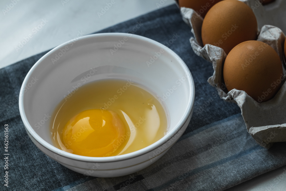 Broken chicken egg in a white plate near a chicken box on a gray napkin. Broken chicken egg in a white plate near a chicken box on a gray napkin.