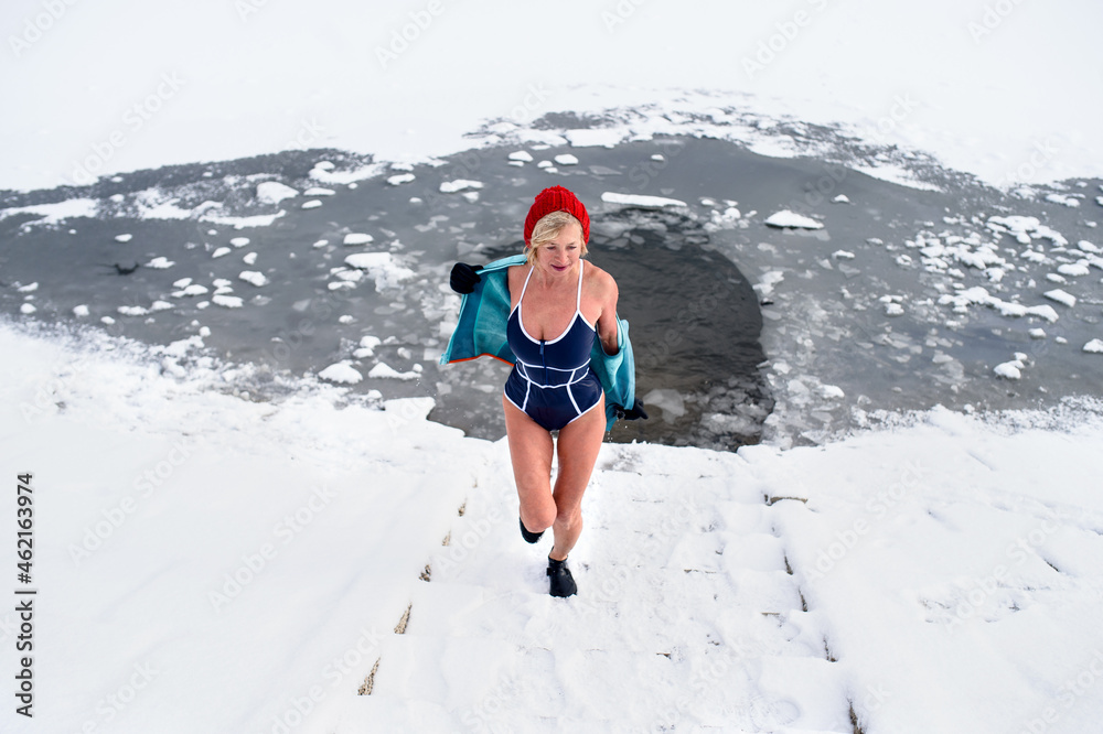 High angle view of active senior woman in wet swimsuit running up stairs outdoors in winter, cold therapy concept.
