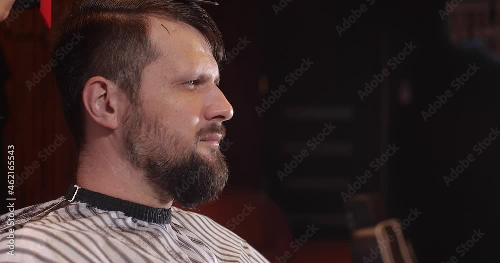 Close-up of a handsome Caucasian guy sitting in a hairdressing salon. An unrecognizable barber parses hair with a comb. 4K 50 fps slow motion Close-up of a handsome Caucasian guy sitting in a hairdressing salon. An unrecognizable barber parses hair with a comb. 4K 50 fps slow motion