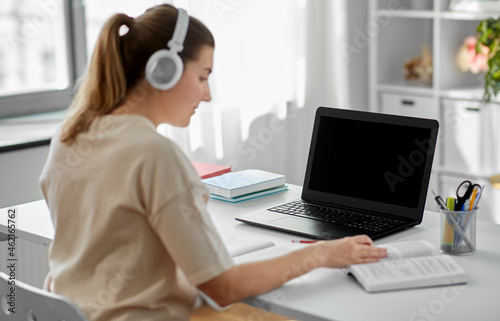 education, online school and distant learning concept - student woman in headphones with laptop computer, notebook and book at home