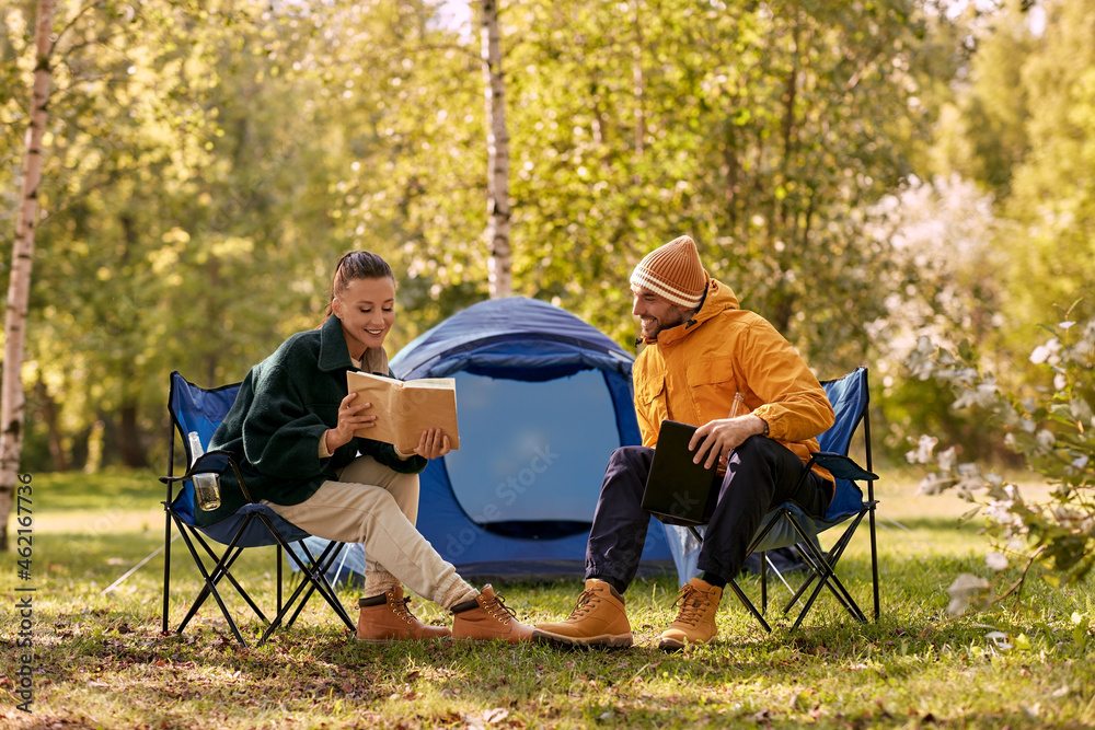 camping, tourism and travel concept - happy couple with tablet pc computer and book resting at tent camp camping, tourism and travel concept - happy couple with tablet pc computer and book resting at tent camp