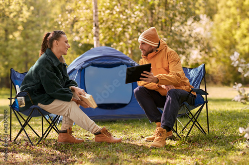 camping, tourism and travel concept - happy couple with tablet pc computer and book resting at tent camp #462167948