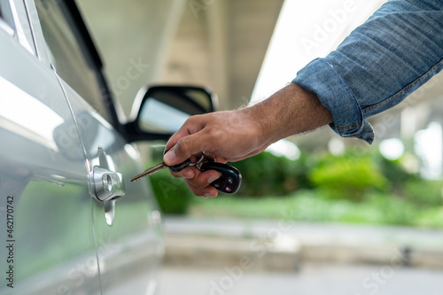 Closes up hand of male key lock or unlock the car door before driving. Vehicle transportation travel of gray car on the street road. Travel concept