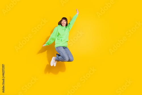 Full length photo of happy cheerful young woman jump up good mood raise hands isolated on yellow color background