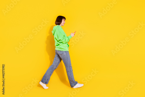 Full length body size profile side view of nice cheery girl going using gadget isolated over bright yellow color background