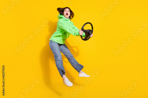 Full size photo of attractive young shocked woman jump up hold steering wheel isolated on yellow color background © deagreez