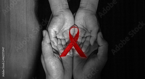 a red ribbon on child's hands held by adult's hands on world aids day. photo