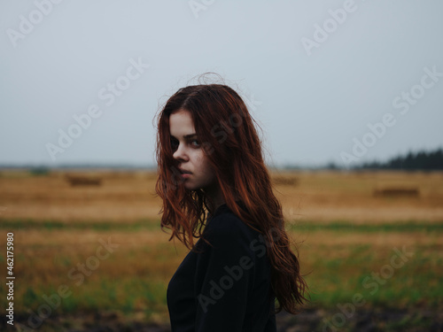 red-haired woman in black dress in a field landscape posing