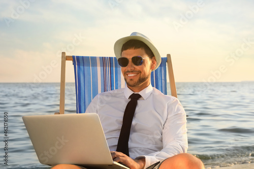 Happy man with laptop on deckchair near sea. Business trip © New Africa