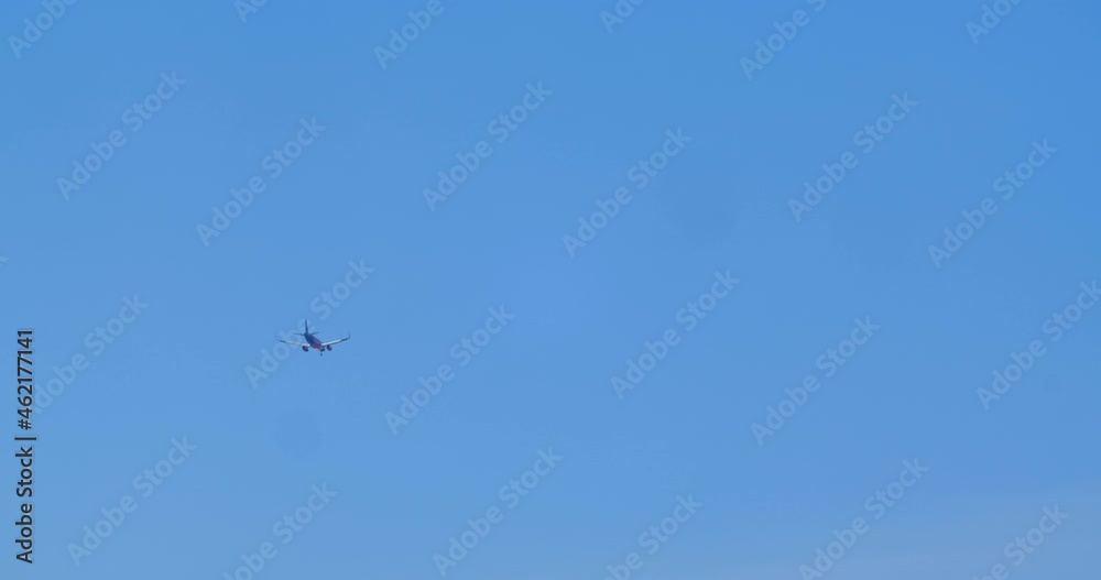 Bottom view from the ground on a passenger plane flying in the distance. A small airliner flies in the distance across the blue cloudless sky. Bottom view from the ground on a passenger plane flying in the distance. A small airliner flies in the distance across the blue cloudless sky.