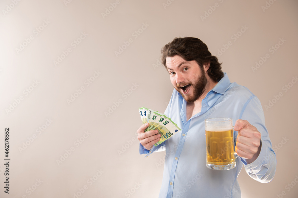 Happy young bearded man with 100 euro banknotes and a beer mug isolated on a gray background Happy young bearded man with 100 euro banknotes and a beer mug isolated on a gray background