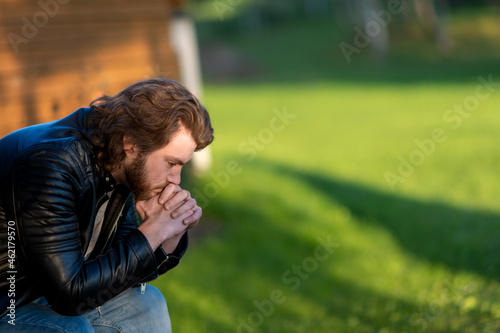 Pensive serious young bearded man wear black leather jacket sitting and thinking outdoors © Zelma