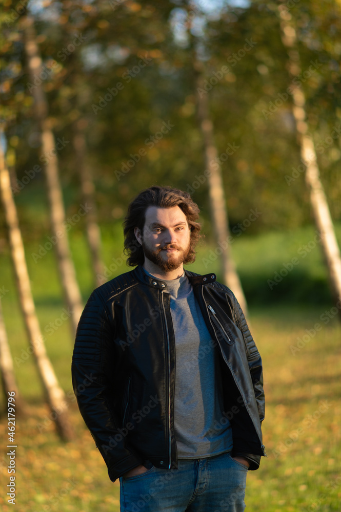 Young bearded man standing and looking at camera against a background of colorful autumn trees Young bearded man standing and looking at camera against a background of colorful autumn trees