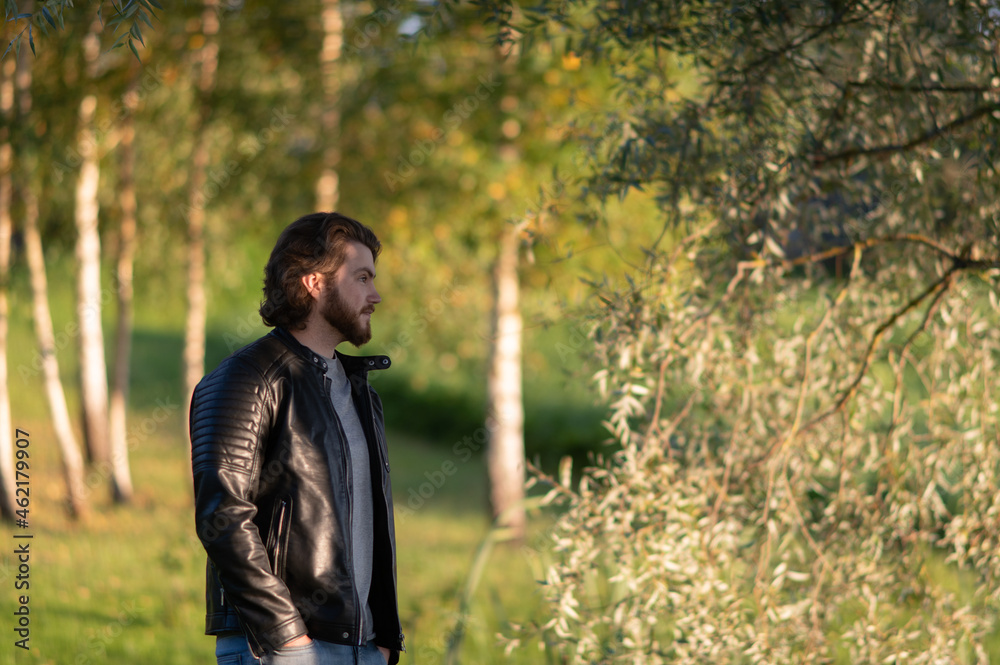 Side view of a young thoughtful bearded man in a black leather jacket, outdoor portrait Side view of a young thoughtful bearded man in a black leather jacket, outdoor portrait