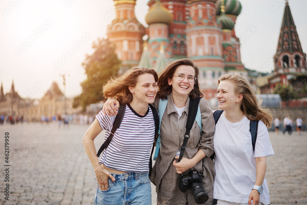 Three young women friends happily walking along Red Square in Moscow
