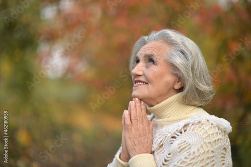 Portrait of beautiful senior woman praying outdoors in autumn