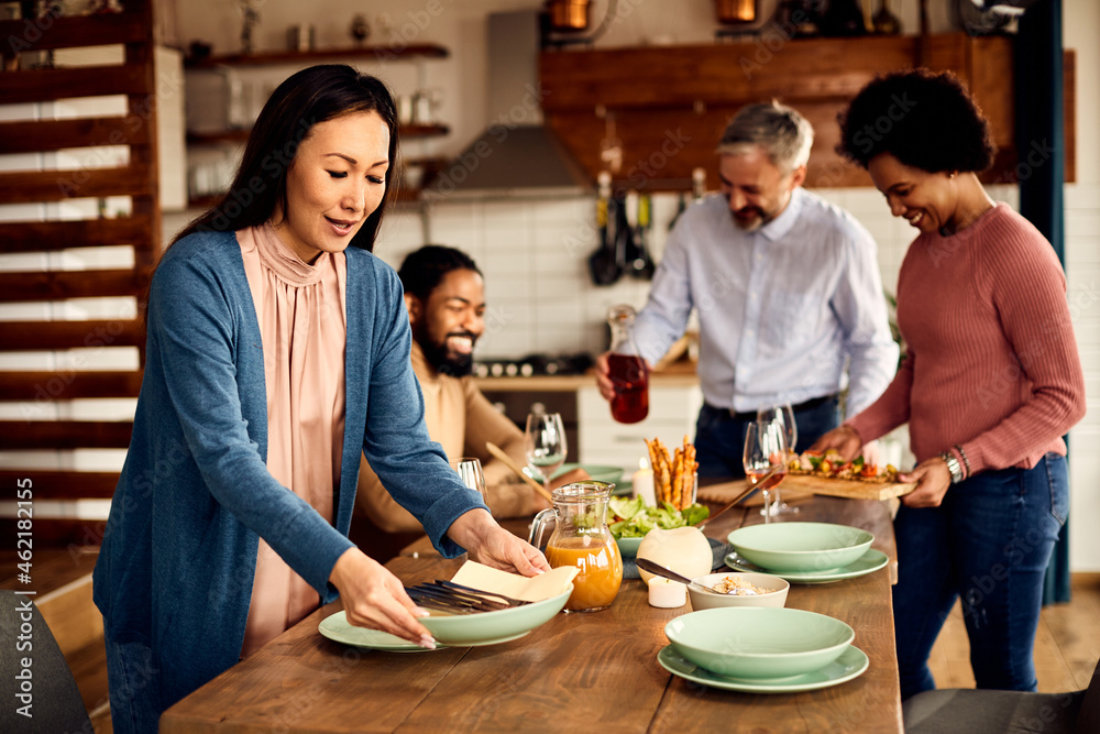 Group of happy multi-ethnic friends setting dining table for lunch at home. Group of happy multi-ethnic friends setting dining table for lunch at home.