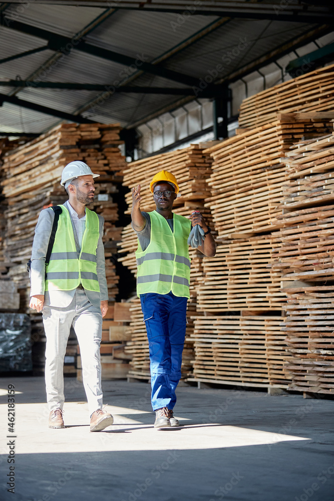 African American lumber worker talks to his manager while walking through warehouse.