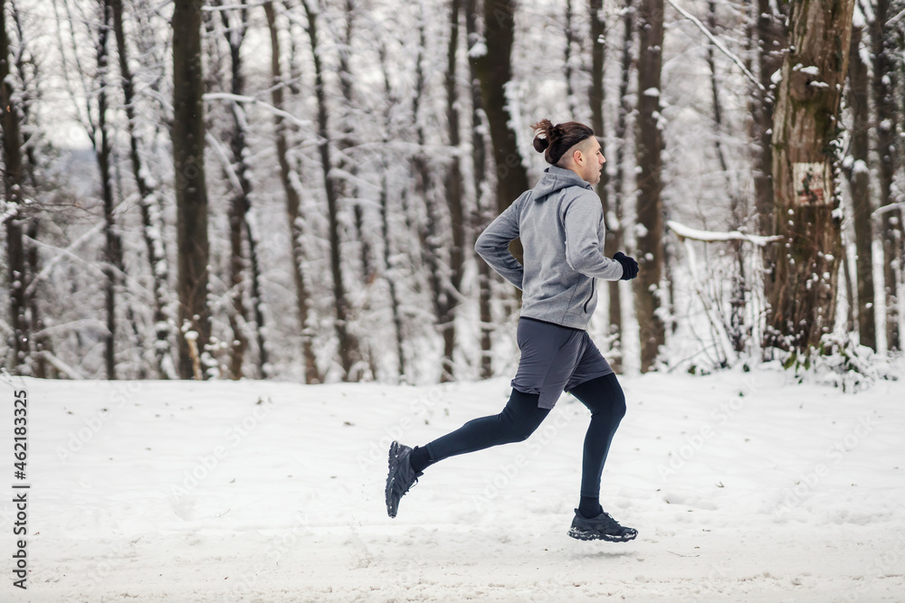 Sportsman running in woods at snowy winter day. Cardio exercises, winter fitness, outdoor fitness