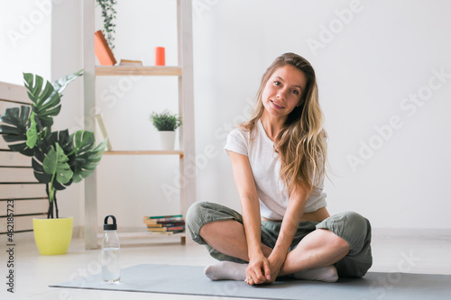Fototapeta Naklejka Na Ścianę i Meble -  Positive girl sitting on fitness mat resting after pilates or yoga practice. Mindfulness and wellbeing concept.
