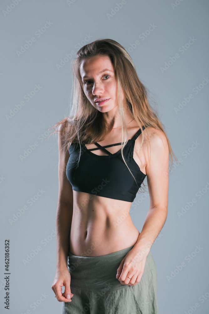 Naklejka premium Fitness and diet concept. Portrait of young woman with perfect sporty body and pretty flat abs in sexy sportswear top on gray background.