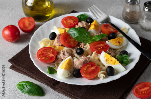 Canned tuna salad with pasta, cherry tomatoes, black olives, boiled egg and basil. Close-up