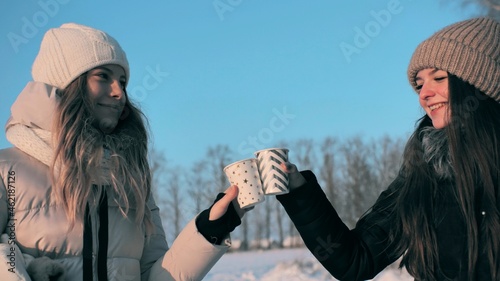 Two friends drink hot tea in winter and clink glasses.