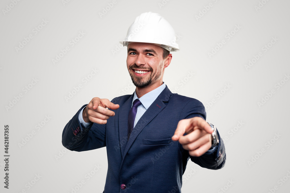Happy businessman in hardhat pointing at camera