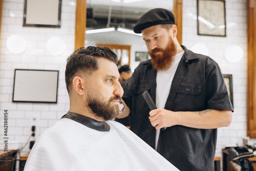 Obraz premium Man getting haircut at the barbershop. Professional barber at work process. Beauty, selfcare, style, fashion, healthcare and male cosmetics concept.