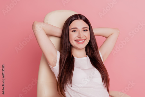Vertical portrait of pretty young happy smiling lady sitting on a chair rest relax comfort cozy isolated over pink color background