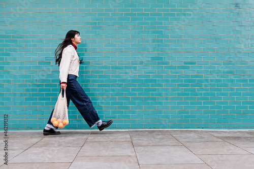 Young woman with mesh bag on footpath by turquoise brick wall photo